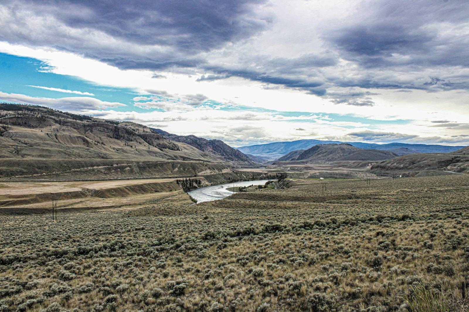 A dry river valley with sagebrush and hills under a wide cloudy sky