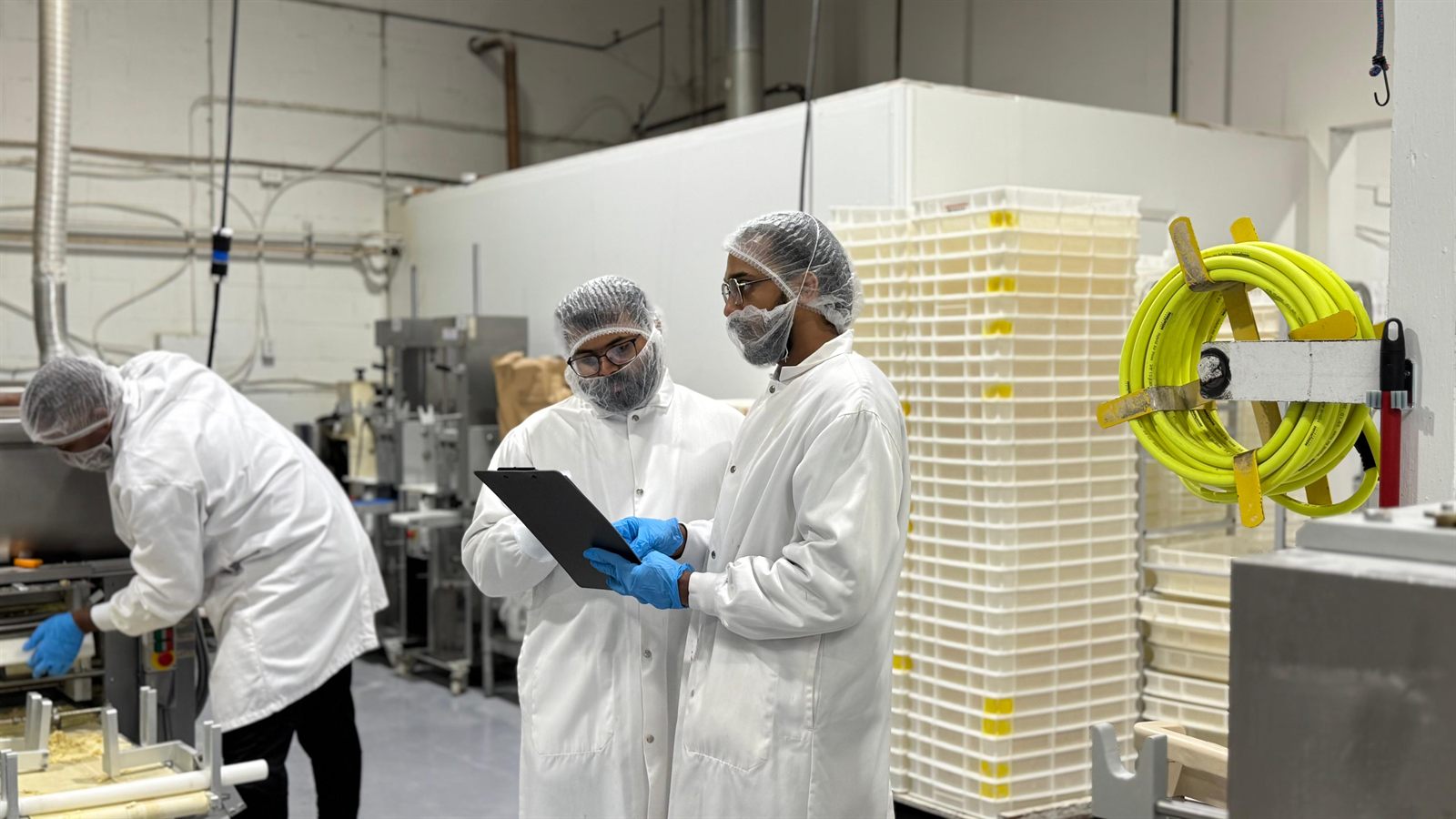 Thomas Kunjumon and a colleague in hairnets, beard nets and white coats reviewing a clipboard on a food production floor